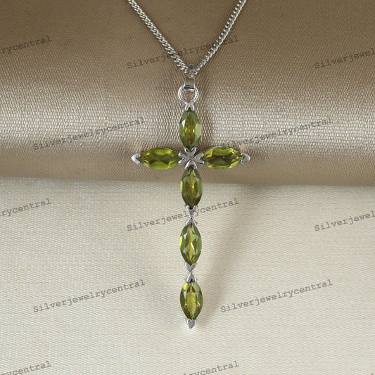 A silver cross pendant necklace featuring four olive green marquise-cut gemstones, displayed on a beige satin fabric background with repeating 'Silverjewelrycentral' watermarks.